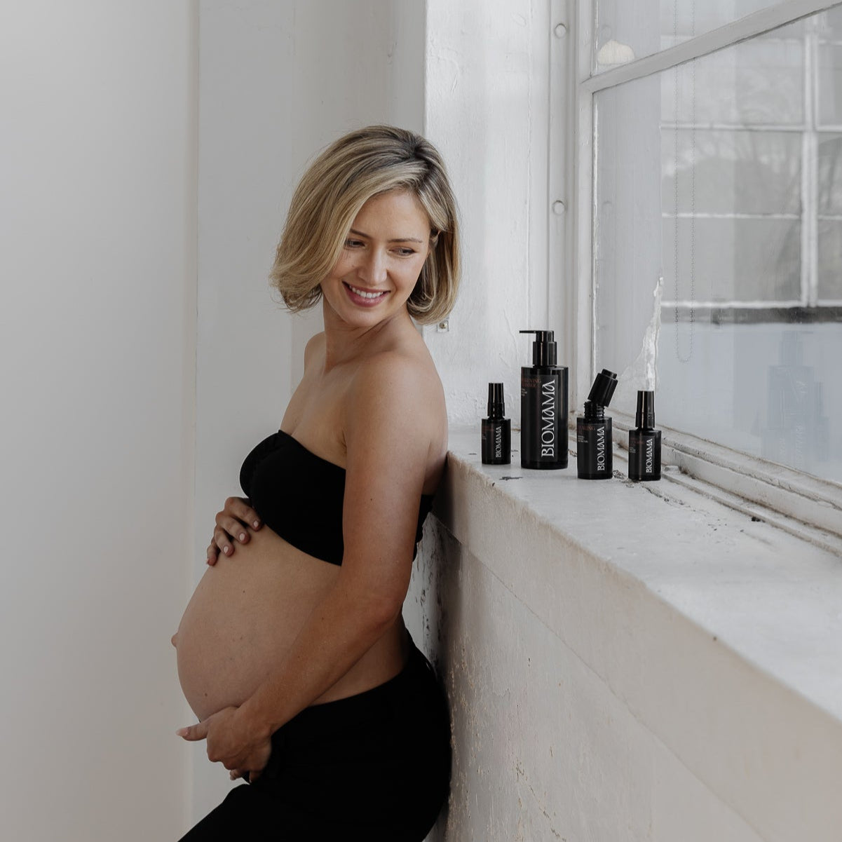 Young pregnant woman holding her belly and standing with Biomama's Essentials Reimagined