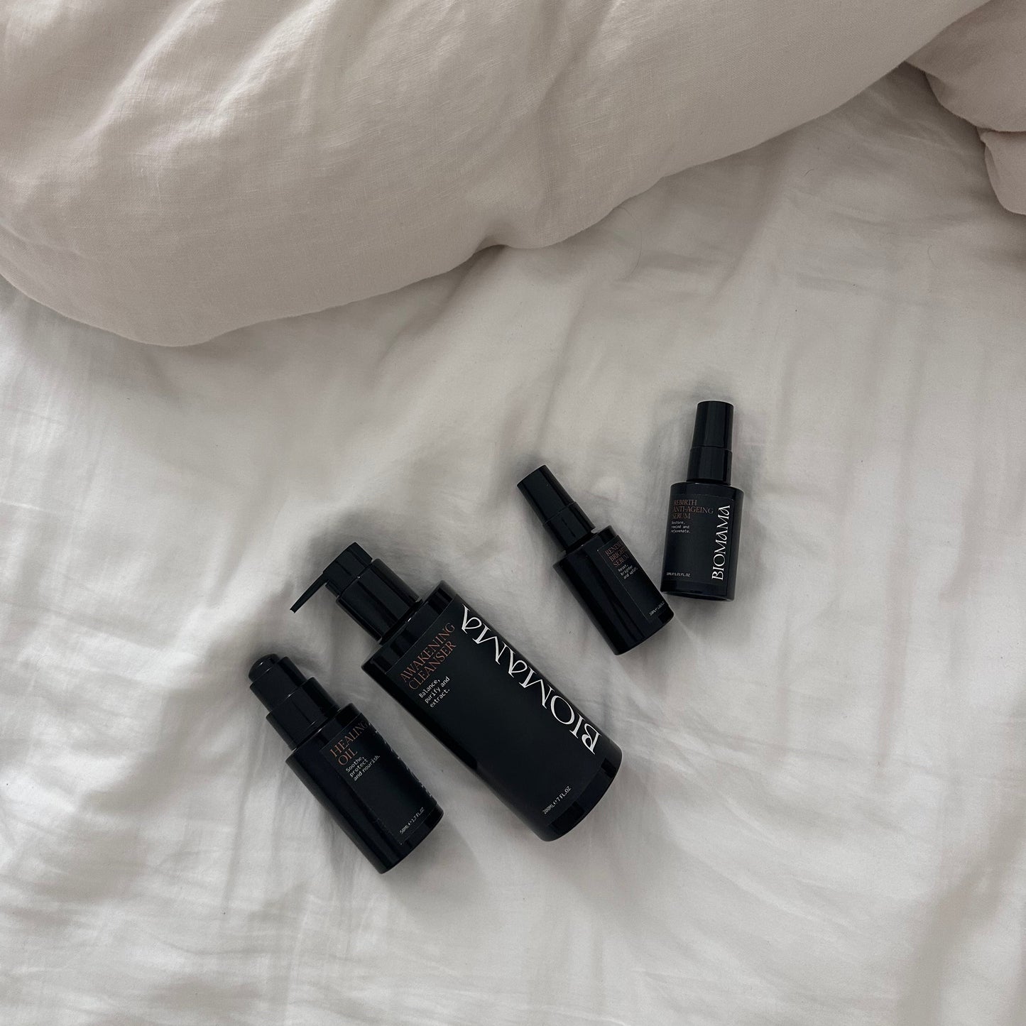 Biomama Skincare's Essentials range containing 4 products is laid out on natural cotton sheets as a lifestyle image and leans in to Biomama's commitment to luxury and natural skincare.